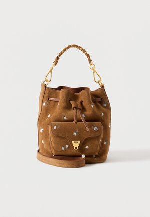 Sac seau en daim marron avec petite broderie de fleur blanche, poignée tressée avec fermoirs dorés, poche avant avec fermoir doré et bandoulière amovible.