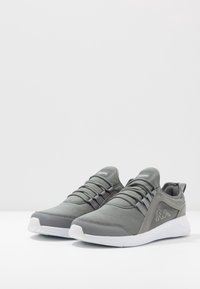 Grå Kappa sneakers med hvide såler, detaljer i net og ruskind, elastiske snørebånd og logo på siden, vist mod en hvid baggrund.