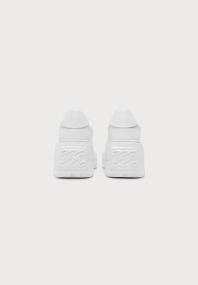 Ζευγάρι λευκά sneakers με πλατφόρμα, εμφανιζόμενα από πίσω, με ανυψωμένη σόλα και ανάγλυφο λογότυπο στη φτέρνα.