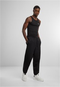 Schwarzes Tanktop und lockere schwarze Jogginghosen mit elastischen Bündchen. Weiße Sneaker runden das Outfit ab. Minimalistisches Design mit Logodetails.