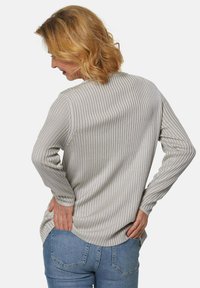 Hellgrauer, gerippter Langarmshirt mit strukturiertem Stoff und abgerundetem Saum. Kombiniert mit blauer Denim, was eine lockere Passform zeigt.