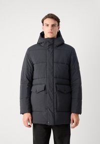 Dark puffer jacket featuring a hood, front zipper, two flap pockets, and a quilted design. Made of lightweight, water-resistant material.