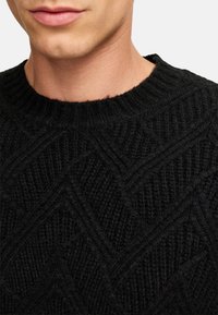 Schwarzer Strickpullover mit einem strukturierten Zickzackmuster und einem gerippten Rundhalsausschnitt. Das Material wirkt weich und dick.