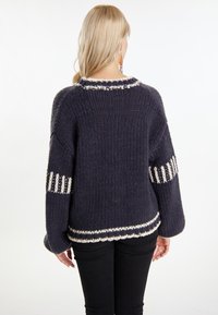Kuscheliger navyfarbener Pullover mit cremefarbenen Akzentstreifen, gestrickter Textur, weiten Ärmeln und runder Ausschnittform. Die Rückansicht zeigt einen gerippten Abschluss.