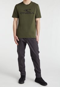 Camiseta verde oliva con un logo negro de "O'Neill", combinada con pantalones gris oscuro y zapatos negros con cordones. El ajuste es casual y relajado.