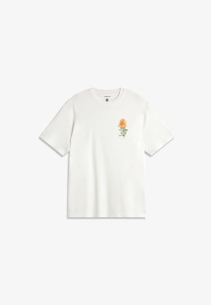 T-shirt blanc à manches courtes avec un petit graphique de fleur orange et tige verte sur le côté gauche de la poitrine, avec le texte « FAITES UN JARDIN » sous la fleur.