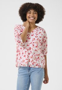 Blusa floreale rosa con maniche corte, scollo a V, vestibilità ampia, tessuto texture, piccoli fiori rossi, abbinata a jeans blu.