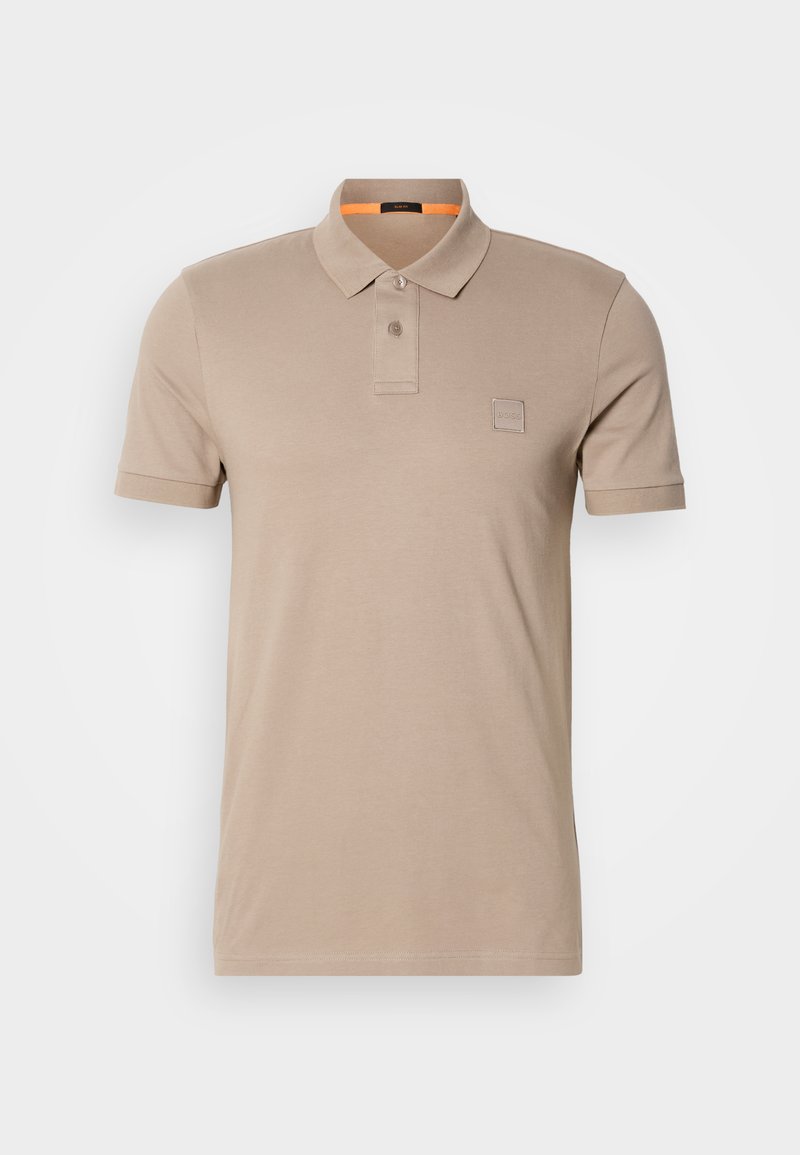 Polo beige en coton, avec un col à deux boutons, des manches courtes et un discret logo sur la poitrine. Intérieur du col accentué en orange.