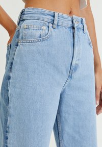 Jean en denim bleu clair avec une taille haute, une coupe droite et un léger effet usé. Il comporte des poches avant et une fermeture à bouton.