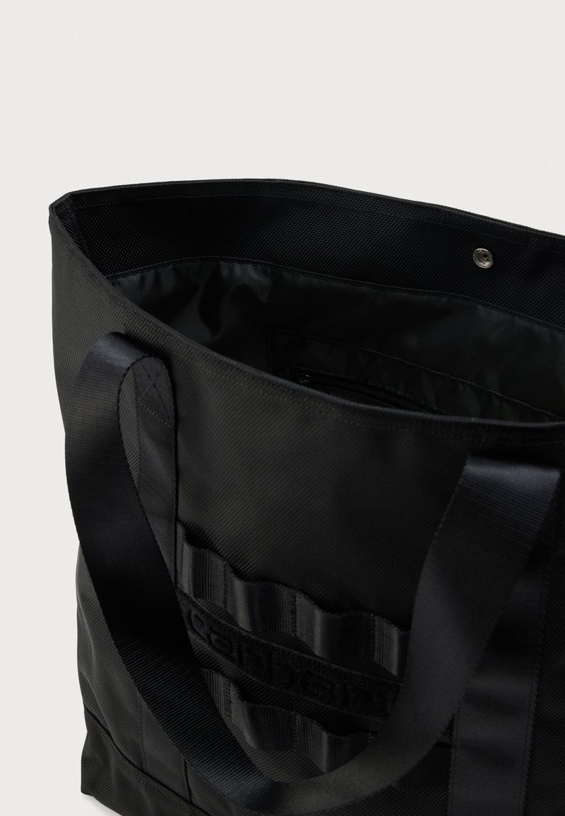 Borsa tote nera con manici larghi, apertura superiore che mostra la tasca interna con cerniera e dettaglio logo esterno cucito.