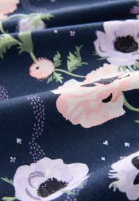 Tissu bleu foncé avec une texture plissée présentant des fleurs rose pâle et blanches avec des tiges vertes et de petits points décoratifs violets.