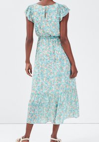 Robe maxi florale bleu clair avec de courtes manches à volants, taille cintrée et ourlet en niveaux. Caractérisée par un dos avec détail en trou de serrure.