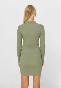 Gebreide jurk in olijfgroen, met lange mouwen, een kraag en een geribbelde textuur, met een aansluitende silhouet die tot halverwege de dij reikt.