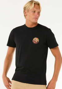 Camiseta de algodón negra con cuello redondo, que presenta un colorido logotipo gráfico circular en el lado izquierdo del pecho. Diseño sencillo, con mangas cortas.