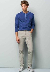 Blauwe langemouwen henley-shirt, ivoorkleurige broek, grijze bootschoenen. Shirt heeft een knoopsluiting; broek is slim-fit met een gladde textuur.