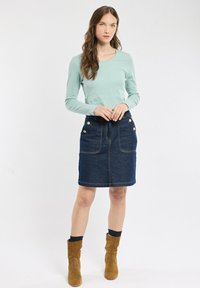 Chemise à manches longues vert clair associée à une jupe en denim bleu foncé avec des boutons dorés et des poches avant, portée avec des bottes chelsea en suède marron.