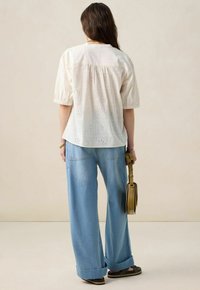 Light cotton blouse with eyelet pattern, short puff sleeves, button closure, paired with high-waisted light blue wide-leg jeans.