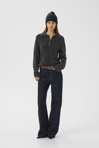 Pulover tricotat gri închis cu guler și nasturi, asociat cu blugi din denim închis la culoare, cu talie înaltă, și o pălărie neagră de tip beanie.