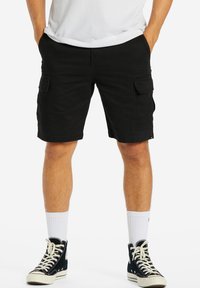 Svarte cargo shorts med flere lommer, detaljeret syning og en komfortabel pasform, parret med sorte høj-top sneakers og hvide sokker.
