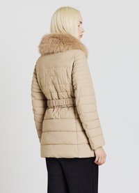 Doudoune beige avec texture matelassée horizontale, col en fourrure, taille élastique et manches longues. Matière lisse, coupe mi-longue.