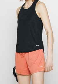 Czarny sportowy top z siateczki zestawiony z koralowymi szortami. Posiada okrągły dekolt i małe logo na obu elementach.