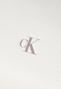 Biela textúrovaná koža s prelisovaným fialovým logom "ck", ktorá predvádza hladký, jemne štruktúrovaný povrch a čistý dizajn.