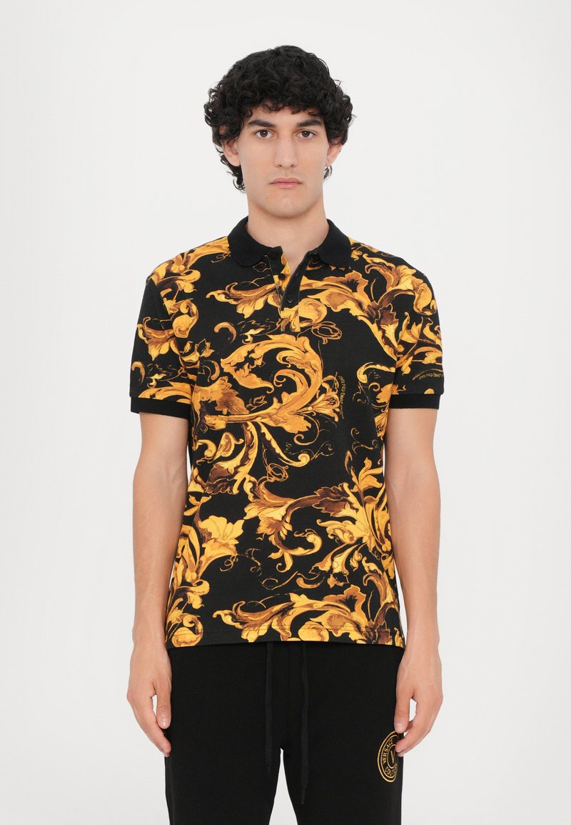 Camisa polo preta com um padrão floral dourado e castanho, mangas curtas e colarinho abotoado. Usada com calças de treino pretas.