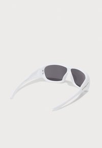 Óculos de sol envolventes brancos com lentes escuras e um logotipo na haste, exibidos sobre uma superfície plana e iluminada.