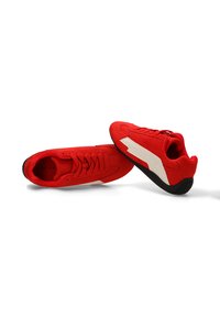 Zapatillas de ante rojo con un acabado texturizado, que presentan una franja de acento blanca, diseño de lazada y suela de goma negra.