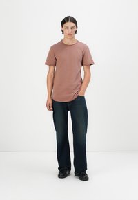 Staubrosa T-Shirt mit kurzen Ärmeln und Rundhalsausschnitt, kombiniert mit dunkelblauen geraden Jeans und schwarzen Schuhen. Einfache, einfarbige Farbtöne.