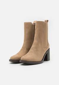 Tan suede ankle boots with a block heel, featuring a side zipper and smooth texture, rounded toe, and minimalist design.