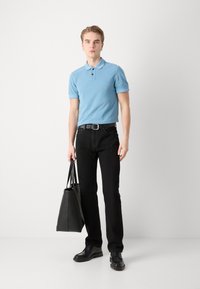Camică polo albastru deschis, cu mâneci scurte, purtată cu blugi negri și pantofi negri. Ținând o geantă tote neagră. Ținută simplă, casual.