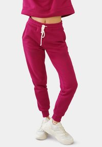 Fuchsia Jogginghosen mit elastischem Bund und Kordelzugdetails, tapered Cuffs und einer weichen Textur, kombiniert mit weißen Sneakers.