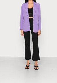 Fioletowa marynarka o dopasowanym kroju, połączona z czarną, krótką koronkową bluzką i czarnymi, rozszerzanymi spodniami. Noszona w duecie z czarnymi sandałami na odsłonięte palce.