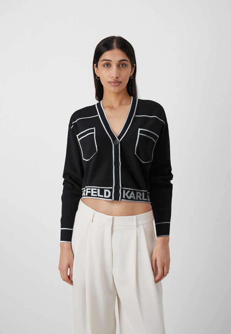Cardigan cropped nero con cuciture bianche a contrasto, chiusura a bottoni e due tasche. Presenta il marchio "KARL" lungo l'orlo.