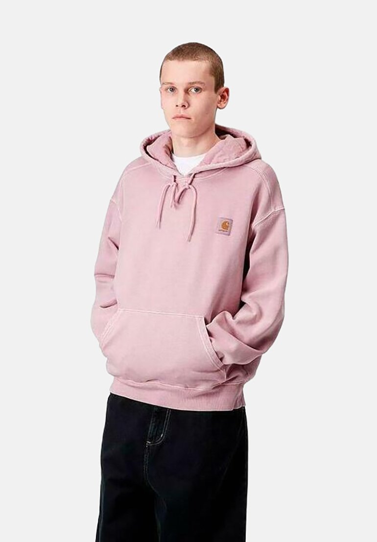 Sudadera con capucha de color rosa claro, con un bolsillo frontal y puños acanalados. Presenta un pequeño parche con el logo en la zona del pecho. Se lleva con pantalones negros.