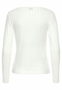 Top bianco a maniche lunghe con texture a coste, caratterizzato da un collo scallop e dettagli delicati a pattern su tutta la stoffa.