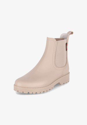 Botte en caoutchouc beige montant à la cheville avec semelle épaisse, panneaux élastiques sur les côtés et languette à l’arrière pour un enfilage facile.