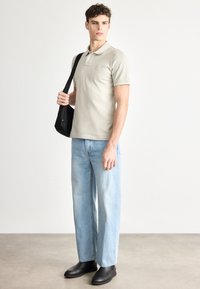 Μπεζ πόλο μπλούζα με κοντά μανίκια και μικρό λογότυπο, συνδυασμένη με τζιν παντελόνι ίσιας γραμμής ανοιχτού χρώματος και μαύρες μπότες αστραγάλου. Μαύρη τσάντα ώμου.