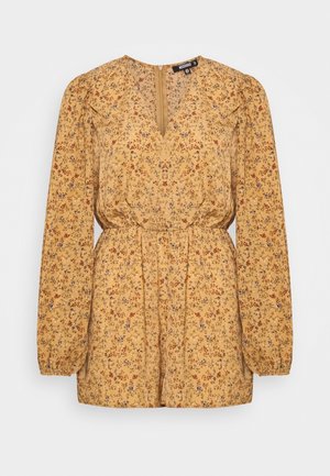 Blouse jaune moutarde à motifs floraux avec manches longues bouffantes, encolure en V, taille froncée et fermeture éclair au dos. Présente de petits motifs floraux rouges et bleus.