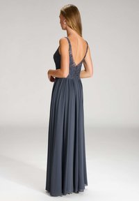 Langes, dunkelgraues Abendkleid mit einem Spitzenoberteil, tiefem V-Ausschnitt auf dem Rücken und fließendem Rock. Dünne Träger schaffen eine zarte Silhouette.
