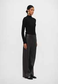 Svart turtleneck genser med tett design. Høyt liv, vide lærbukser i mørkebrunt. Modell som har på seg svarte slip-on sko.