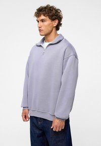 Licht paarse sweatshirt met een halve rits kraag, relaxte fit, verlaagde schouders en geribde manchetten, gecombineerd met donkere jeans.