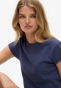 Camiseta de manga corta azul marino en una tela suave con cuello redondo, que presenta una textura lisa y un diseño ligeramente ajustado.