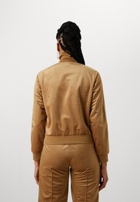 Tan satin Bomberjacke mit hohem Kragen und enganliegenden Bündchen, passende Hose, glatte Textur, minimalistisches Design und keine sichtbaren Muster.