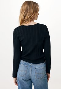 Černý žebrovaný svetr s kulatým výstřihem a dlouhými rukávy, kombinovaný s džínovými kalhotami vysokého pasu v modré barvě a zadními kapsami.