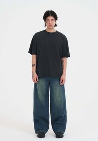 Czarna, oversize t-shirt z odważnym wzorem graficznym, zestawiona z szerokimi spodniami dżinsowymi w ciemnym kolorze, z efektem wyblaknięcia i haftowanymi detalami.