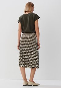 Top verde oliva con maniche corte, abbinato a una gonna midi fantasia con disegni geometrici neri, bianchi e beige.
