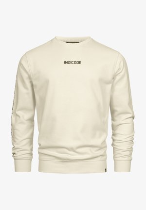 Sudadera color crema hecha de una tela suave, con puños y dobladillo de canalé, presenta el logotipo "INDICODE" en el pecho y detalles impresos en las mangas.