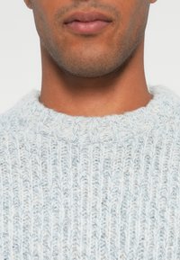Maglione lavorato a maglia blu chiaro con un motivo a costine strutturato e un collo rotondo a girocollo, realizzato in un materiale morbido e peloso.